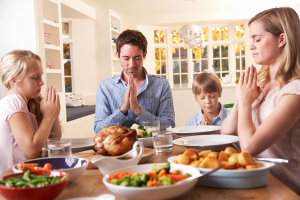 Family Saying Prayer Before Eating Roast Dinner